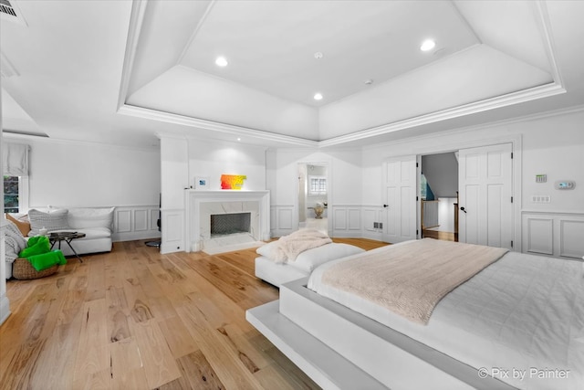 bedroom featuring a raised ceiling, light hardwood / wood-style floors, and a high end fireplace