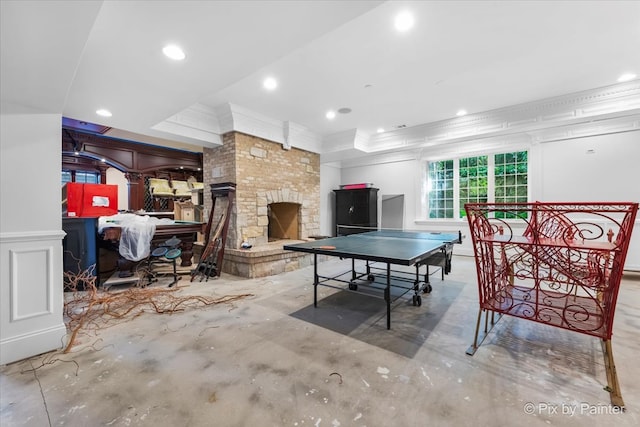 recreation room featuring crown molding, a stone fireplace, and a raised ceiling