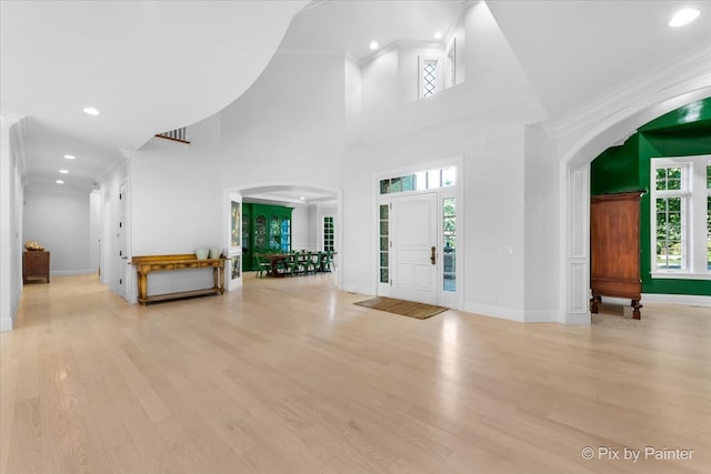 foyer featuring a towering ceiling, light wood-type flooring, and crown molding