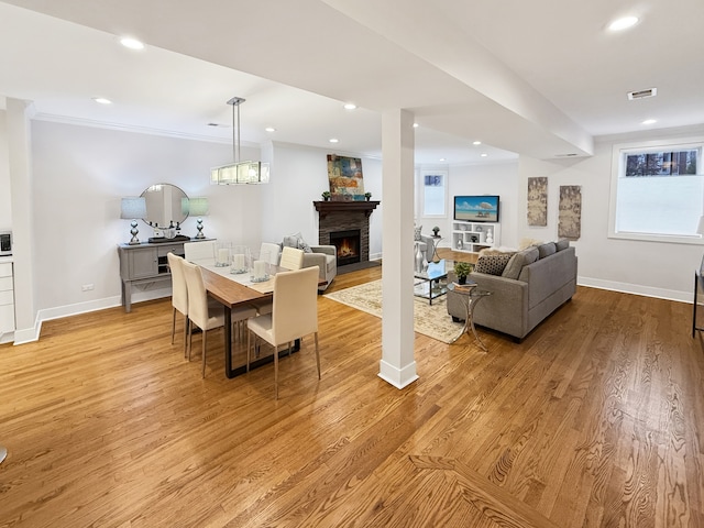 dining space with a fireplace, ornamental molding, and light wood-type flooring