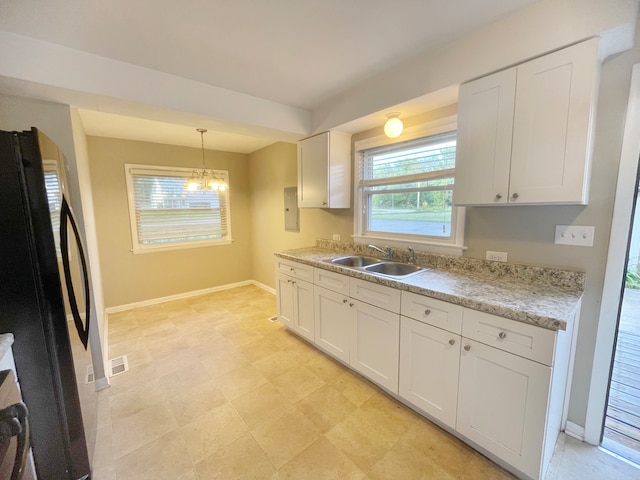 kitchen featuring white cabinets, hanging light fixtures, black fridge, an inviting chandelier, and sink