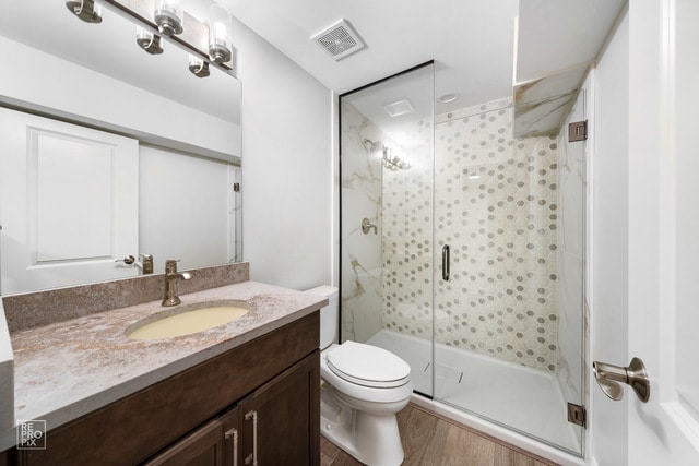 bathroom featuring wood-type flooring, a shower with door, vanity, and toilet