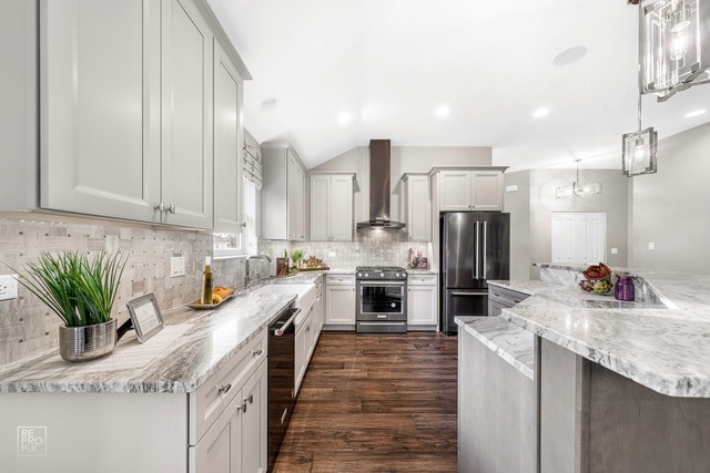 kitchen with decorative light fixtures, wall chimney exhaust hood, stainless steel appliances, light stone countertops, and dark hardwood / wood-style flooring