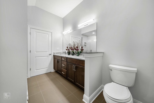 bathroom with tile patterned flooring, vaulted ceiling, vanity, and toilet