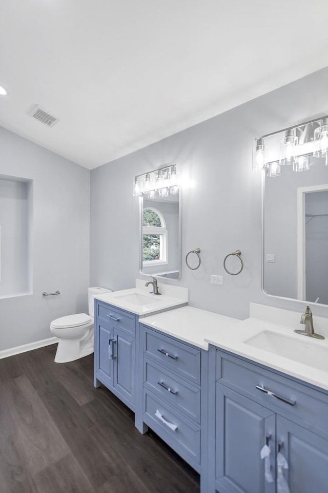 bathroom featuring a sink, double vanity, toilet, and wood finished floors
