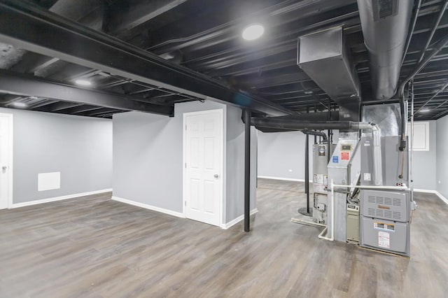 finished basement with heating unit, baseboards, gas water heater, and wood finished floors