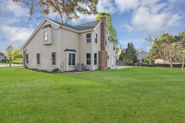 rear view of property featuring a lawn, central air condition unit, a chimney, and fence