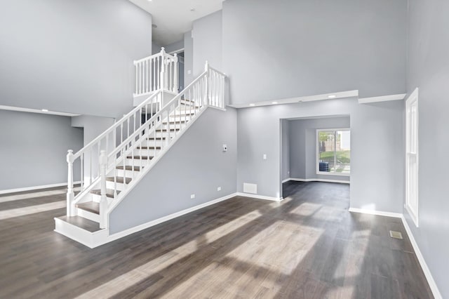 unfurnished living room with baseboards, wood finished floors, stairway, and a towering ceiling
