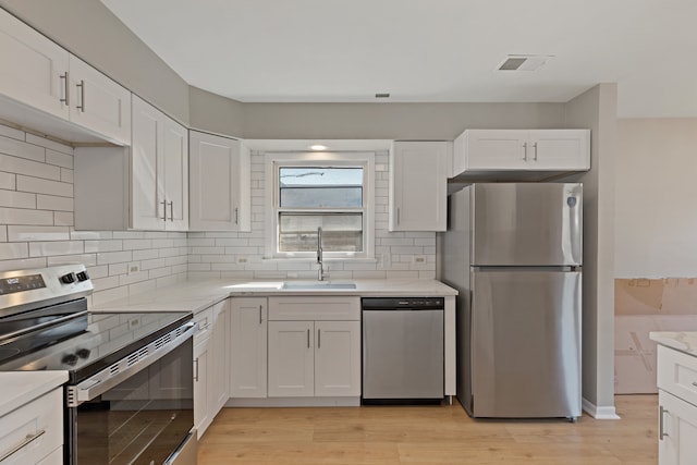 kitchen with appliances with stainless steel finishes, sink, light wood-type flooring, and white cabinetry