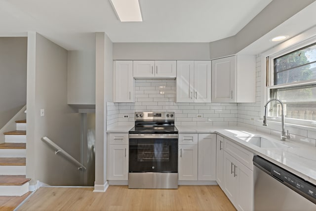 kitchen with white cabinets, backsplash, appliances with stainless steel finishes, and light wood-type flooring