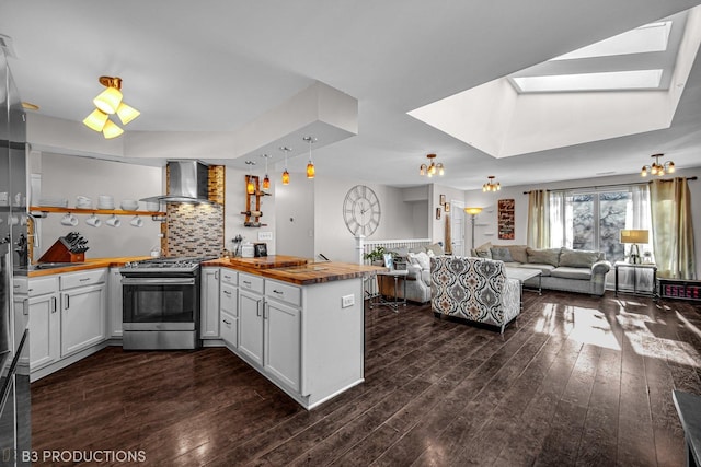 kitchen featuring white cabinetry, stainless steel range with gas stovetop, tasteful backsplash, kitchen peninsula, and wall chimney exhaust hood