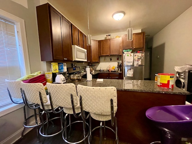 kitchen with appliances with stainless steel finishes, pendant lighting, dark hardwood / wood-style floors, and dark stone counters