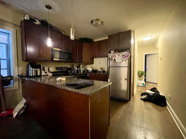 kitchen featuring appliances with stainless steel finishes, dark stone counters, light wood-type flooring, pendant lighting, and dark brown cabinetry