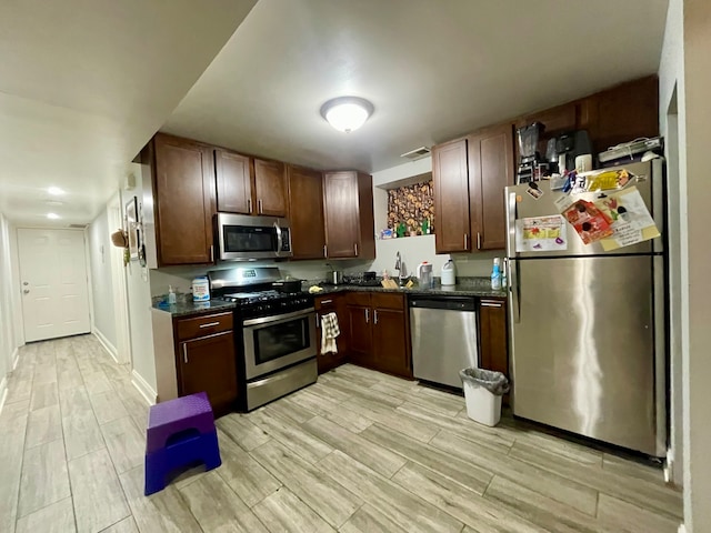 kitchen with sink, appliances with stainless steel finishes, light hardwood / wood-style flooring, and dark stone counters