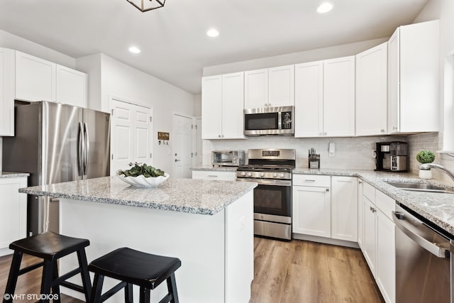 kitchen featuring light hardwood / wood-style floors, white cabinets, sink, a kitchen breakfast bar, and appliances with stainless steel finishes