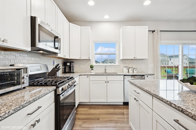 kitchen featuring light hardwood / wood-style floors, sink, appliances with stainless steel finishes, backsplash, and white cabinets