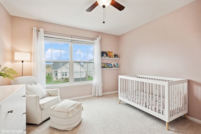 bedroom featuring ceiling fan, a nursery area, and light colored carpet