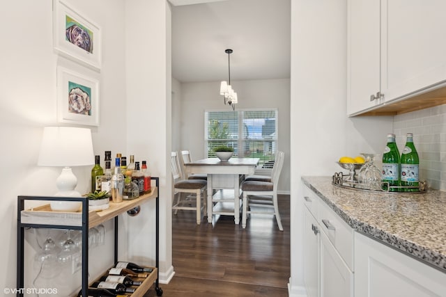 kitchen with decorative backsplash, dark hardwood / wood-style floors, light stone countertops, white cabinetry, and decorative light fixtures