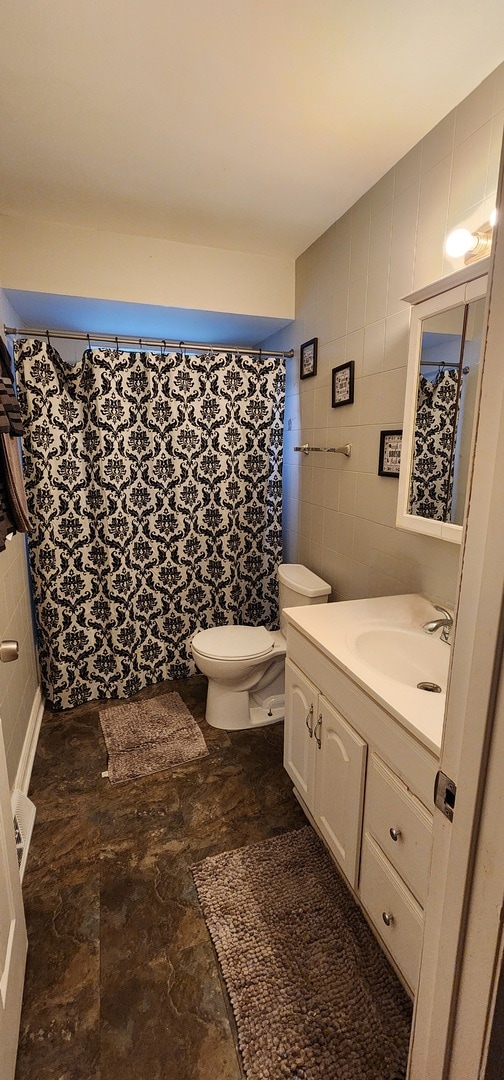 bathroom featuring vanity, tile walls, and toilet