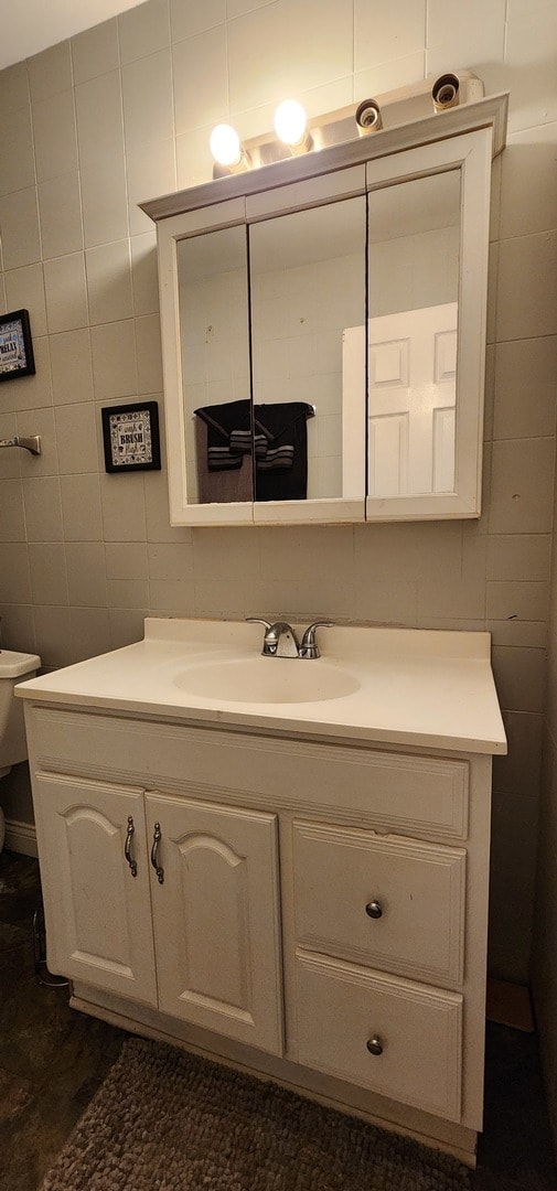 bathroom featuring toilet, vanity, and tile walls