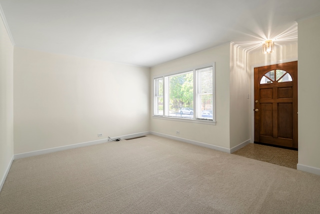 foyer with ornamental molding, a chandelier, and light colored carpet