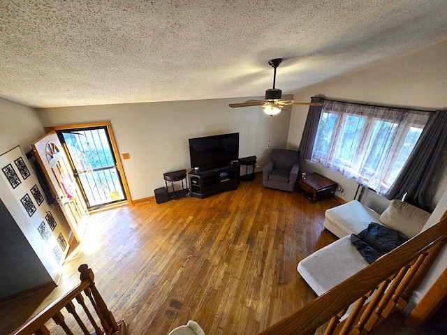 living room with a textured ceiling, hardwood / wood-style flooring, ceiling fan, and vaulted ceiling