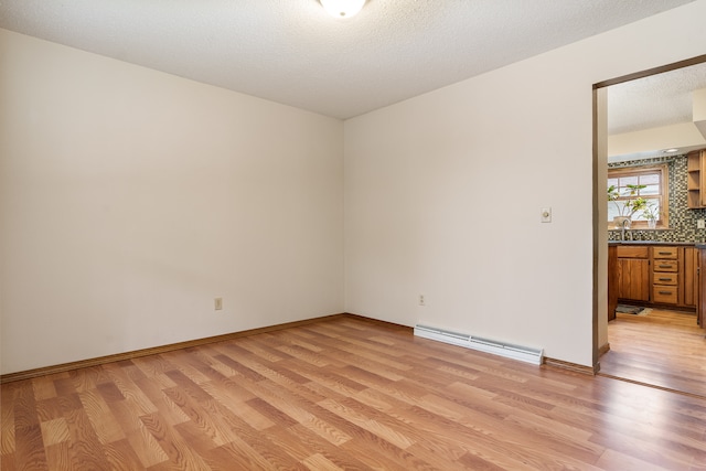 empty room with a baseboard radiator, light hardwood / wood-style flooring, sink, and a textured ceiling