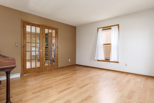 spare room featuring french doors, light hardwood / wood-style floors, a baseboard radiator, and a textured ceiling