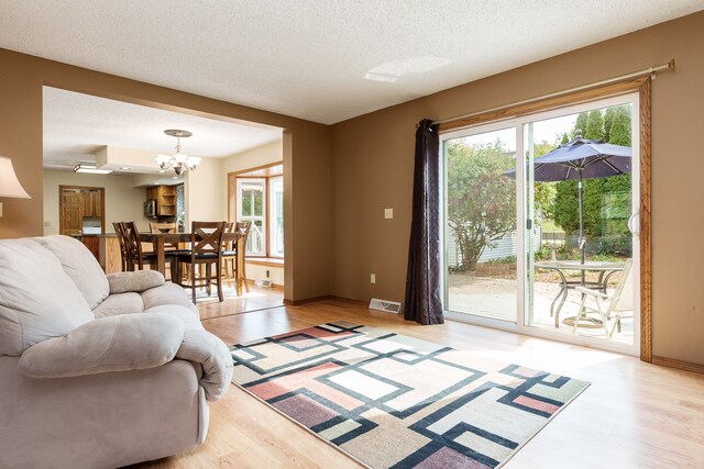 living room featuring a notable chandelier, light hardwood / wood-style flooring, and a textured ceiling