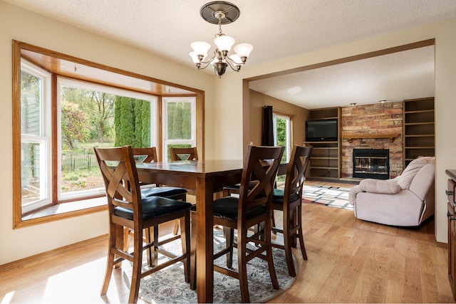 dining area featuring light wood-type flooring, a stone fireplace, an inviting chandelier, and a textured ceiling