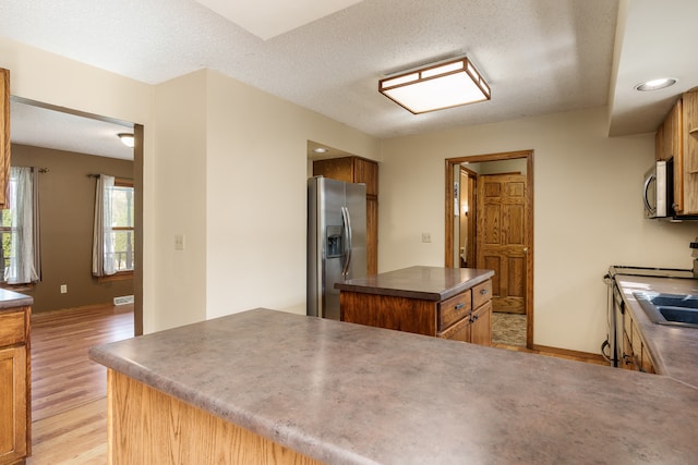 kitchen with a kitchen island, kitchen peninsula, light hardwood / wood-style flooring, appliances with stainless steel finishes, and a textured ceiling