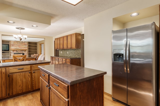 kitchen with decorative light fixtures, backsplash, stainless steel refrigerator with ice dispenser, a center island, and light hardwood / wood-style floors