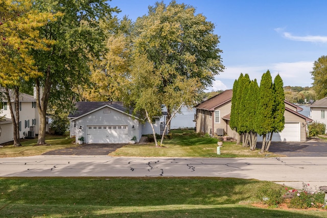 view of property hidden behind natural elements with a garage, cooling unit, and a front lawn