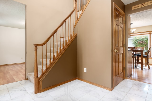 stairway featuring a textured ceiling, a notable chandelier, and hardwood / wood-style flooring