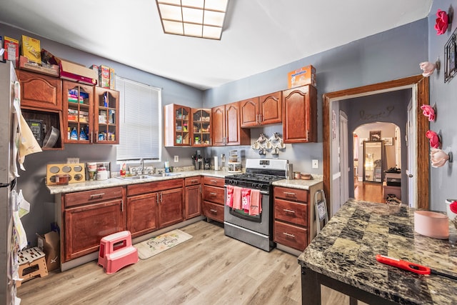 kitchen featuring light wood-type flooring, light stone countertops, sink, and gas range