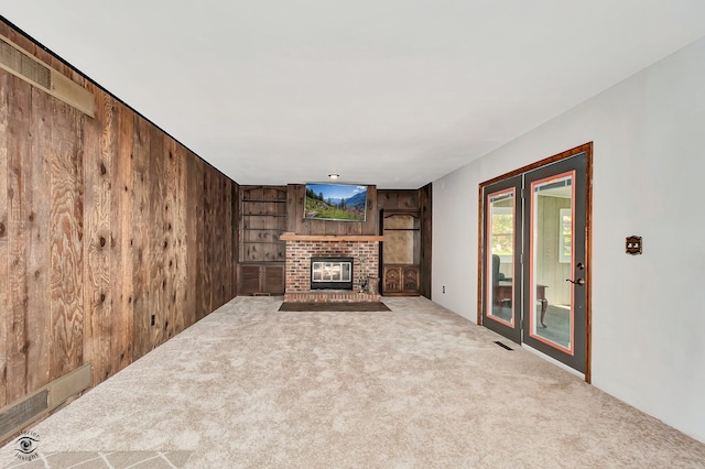 unfurnished living room featuring a fireplace, wood walls, and carpet floors