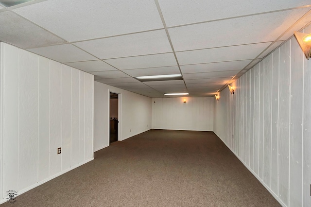 basement with wood walls, a paneled ceiling, and dark colored carpet