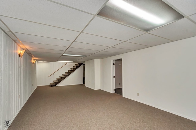 basement featuring carpet floors, wooden walls, and a paneled ceiling