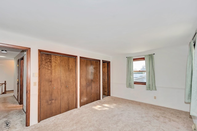 unfurnished bedroom featuring light carpet and multiple closets