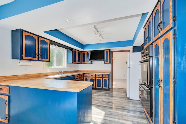 kitchen featuring sink, kitchen peninsula, wall chimney exhaust hood, rail lighting, and light hardwood / wood-style floors