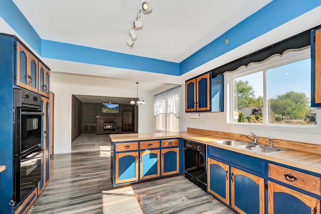 kitchen with pendant lighting, sink, kitchen peninsula, black appliances, and light wood-type flooring