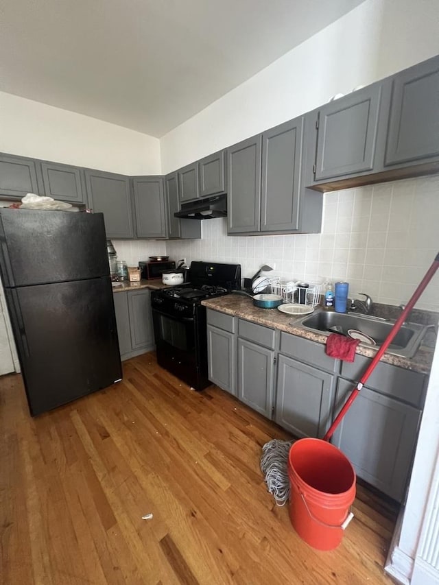 kitchen with black appliances, a sink, wood finished floors, and under cabinet range hood