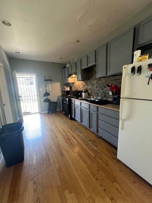 kitchen featuring gas stove, light hardwood / wood-style floors, white refrigerator, gray cabinets, and backsplash