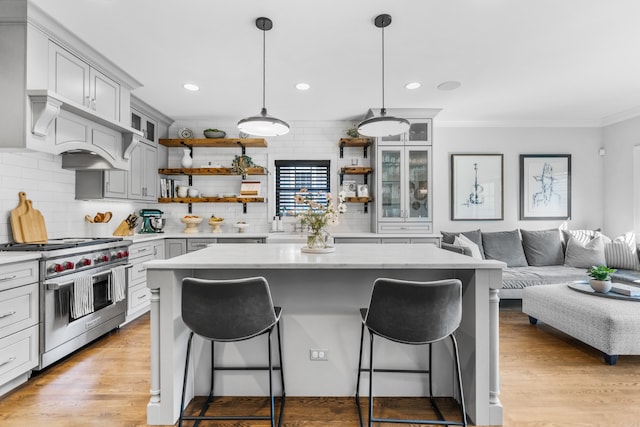 kitchen with range with two ovens, a center island, hanging light fixtures, light hardwood / wood-style floors, and a breakfast bar