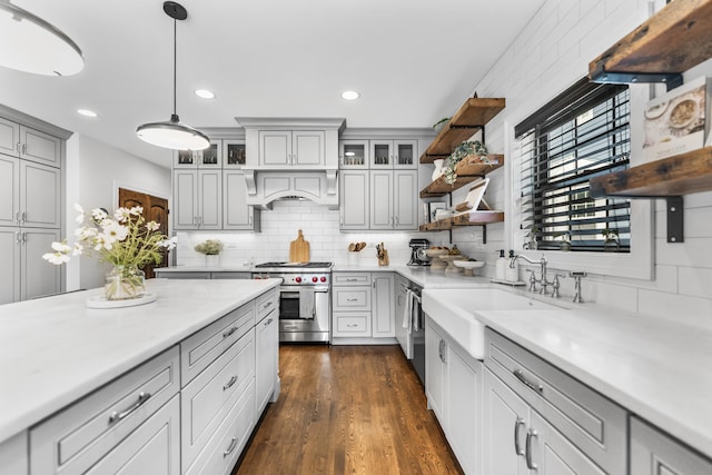 kitchen featuring dark wood-type flooring, custom range hood, decorative light fixtures, appliances with stainless steel finishes, and tasteful backsplash