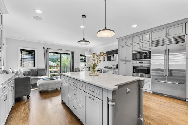 kitchen featuring built in appliances, gray cabinetry, wood-type flooring, crown molding, and pendant lighting