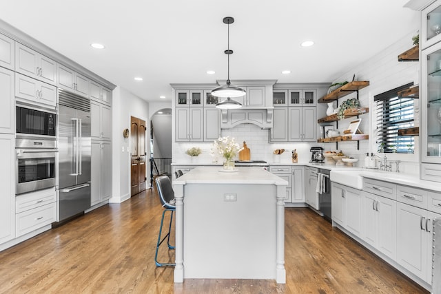 kitchen featuring built in appliances, hardwood / wood-style flooring, a center island, and hanging light fixtures