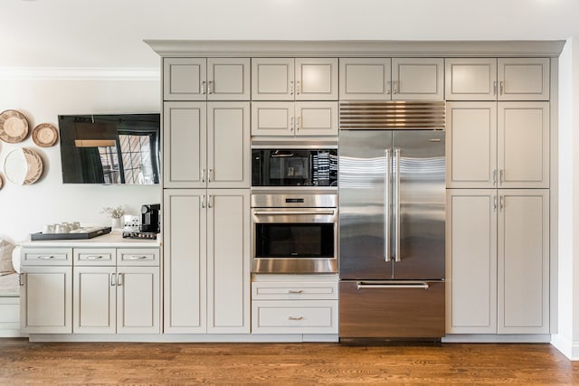 kitchen featuring built in appliances, crown molding, and hardwood / wood-style floors