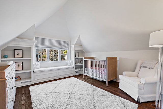 bedroom with lofted ceiling, a crib, and dark wood-type flooring