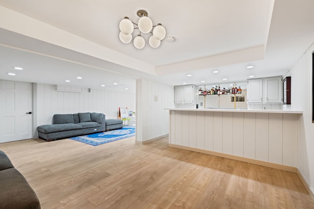 living room featuring bar, a tray ceiling, and light wood-type flooring